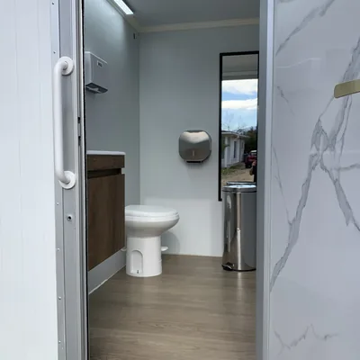 Interior del baño móvil Maihue visto desde la puerta abierta, con revestimiento tipo mármol y piso de madera
