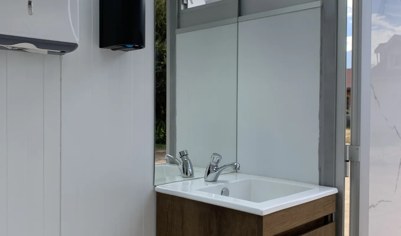 Interior de un tráiler de baños Maihue: vanitorio de madera con lavamanos, grifería, espejo amplio y luz natural