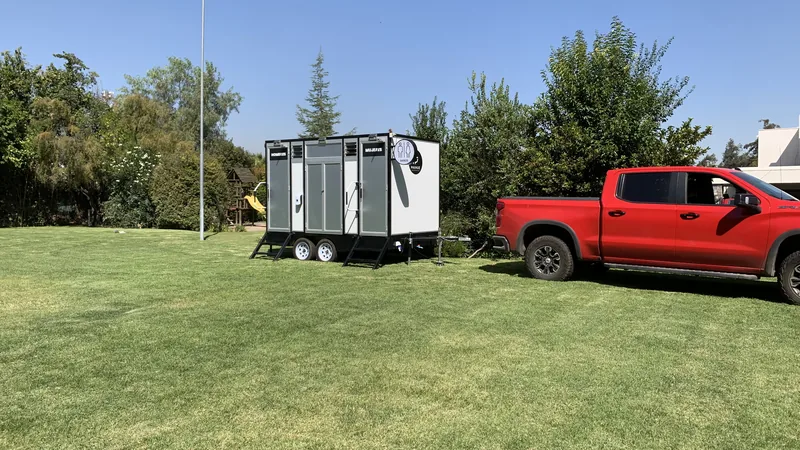 Tráiler de baños móviles premium Maihue instalado en el césped de una parcela, con la camioneta de traslado estacionada al lado