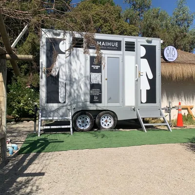 Tráiler de baños móviles Maihue instalado junto a un quincho de techo de paja en una parcela