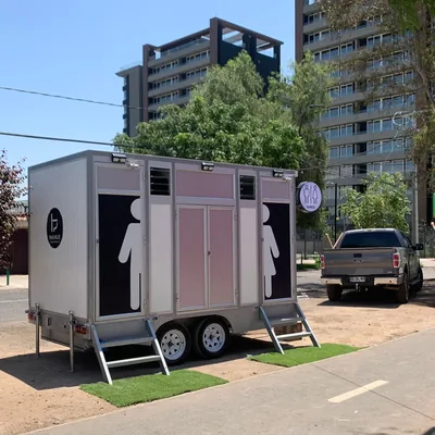 Tráiler de baños móviles Maihue con puertas señalizadas, instalado en una calle de Santiago con edificios al fondo